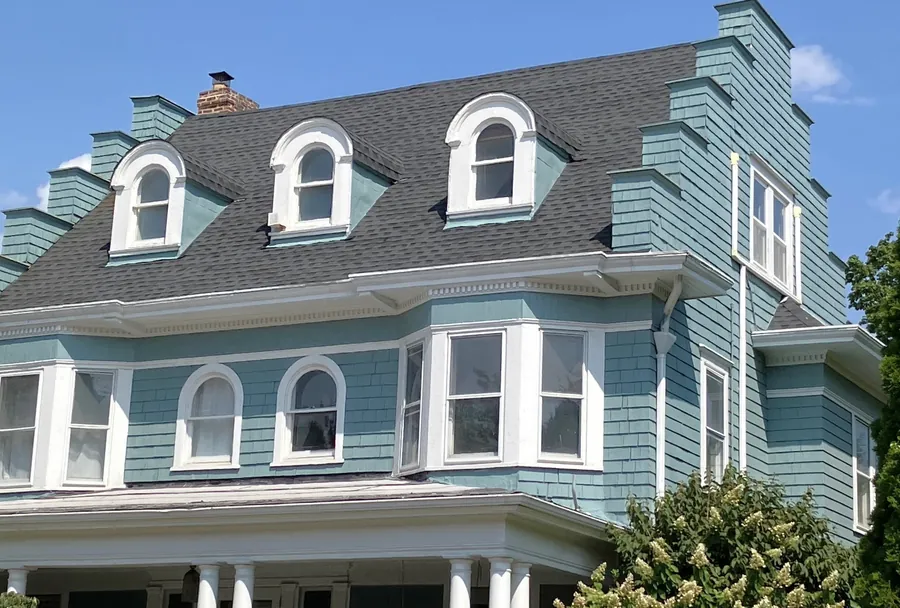 Gray-shingled Victorian-style house with arched dormer windows and a front porch